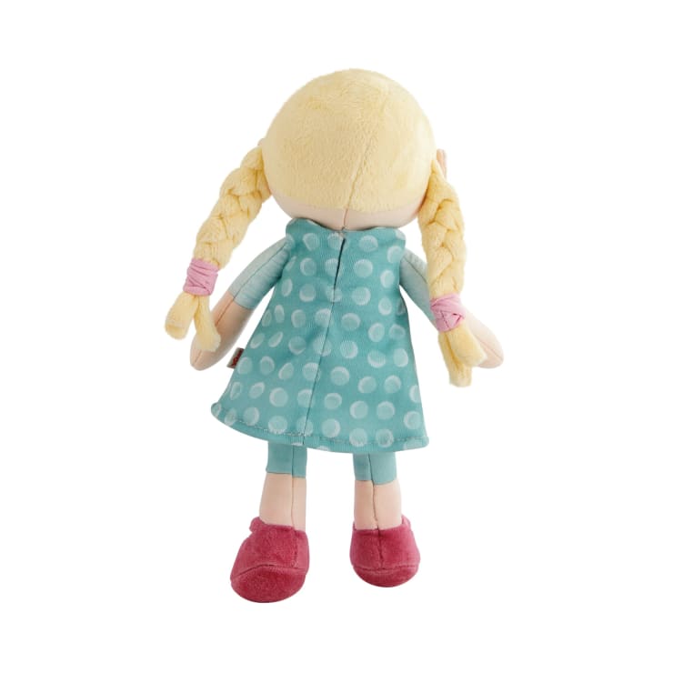 Eine Plüschpuppe, von hinten gesehen, mit blondem, geflochtenem Haar, das mit rosa Bändern zusammengebunden ist. Sie trägt ein blaugrünes Kleid mit weißen Tupfen, blaugrüne Leggings und rosa Schuhe.