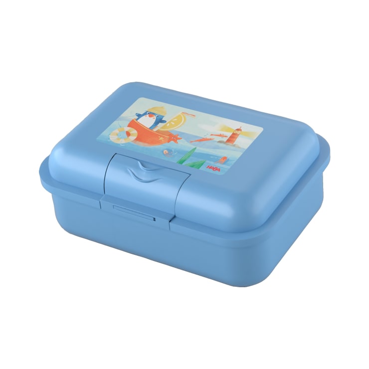 Eine rechteckige blaue Plastik-Lunchbox mit einem Scharnierdeckel, der auf der Oberseite eine Illustration eines Bären und eines Vogels auf einem Boot und einem Leuchtturm zeigt. Die Box hat einen Verschluss auf der Vorderseite für einen sicheren Verschluss.