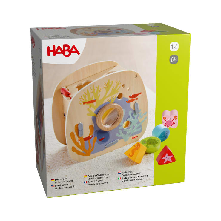 In einer HABA-Markenschachtel befindet sich ein Sortierspielzeug aus Holz mit einem Unterwasserthema, das bunte Meerestiere und geometrische Formen zeigt. Auf der Schachtel ist angegeben, dass das Spielzeug für Kinder ab 18 Monaten geeignet ist und sechs Teile enthält.