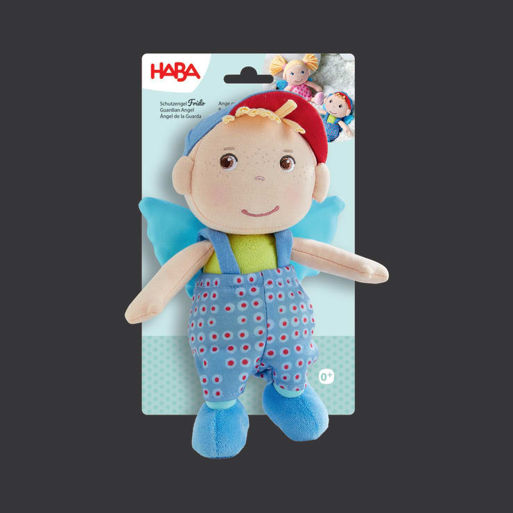 Eine Plüschpuppe mit blauem Overall, grünem Hemd, blauen Flügeln und einem rot-blauen Hut, die auf einer Verpackung mit der Aufschrift HABA abgebildet ist. Die Puppe hat gestickte Gesichtszüge und ist für kleine Kinder gedacht.
