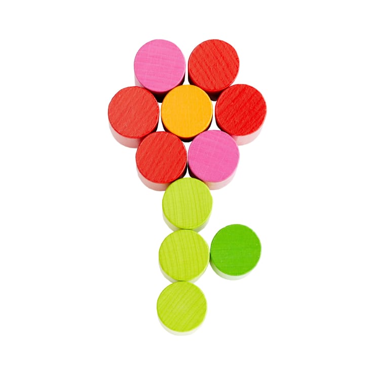 Neun farbige Holzscheiben sind auf weißem Hintergrund so angeordnet, dass sie eine einfache Blumenform bilden, mit roten und rosa Scheiben als Blütenblätter, einer orangefarbenen Mitte und gelben und grünen Scheiben als Stiel und Blatt.
