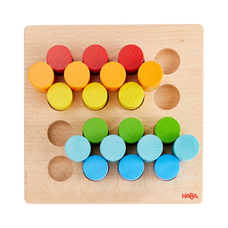 Ein Holzbrett mit vier Reihen von farbigen Zylindern - rot, orange, gelb, grün und blau -, die in die entsprechenden Löcher gesteckt werden. Das HABA-Logo befindet sich in der unteren rechten Ecke.
