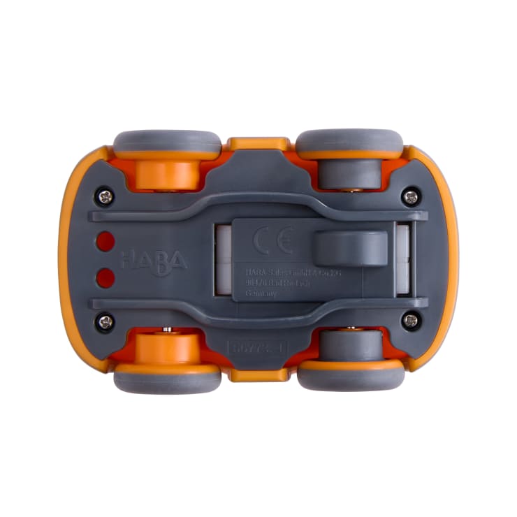 Die Unterseite eines Spielzeugautos mit vier Rädern, einer orange-grauen Farbgebung, sichtbaren Schrauben, roten Lichtern und geprägten Herstellerangaben, dargestellt auf weißem Hintergrund.