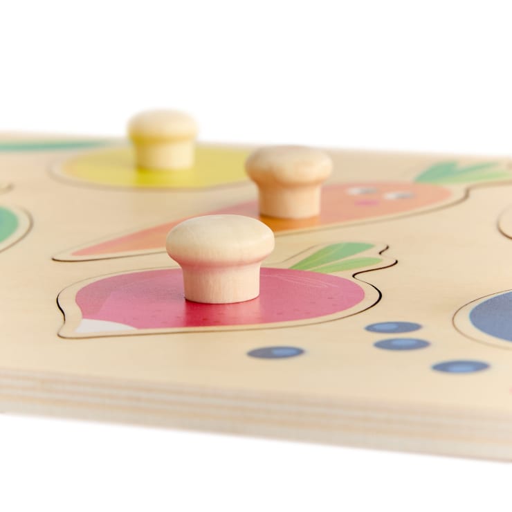 Eine Nahaufnahme eines hölzernen Puzzlebretts mit Knöpfen und bunten Abbildungen von Gemüse, darunter ein Rettich und eine Karotte.