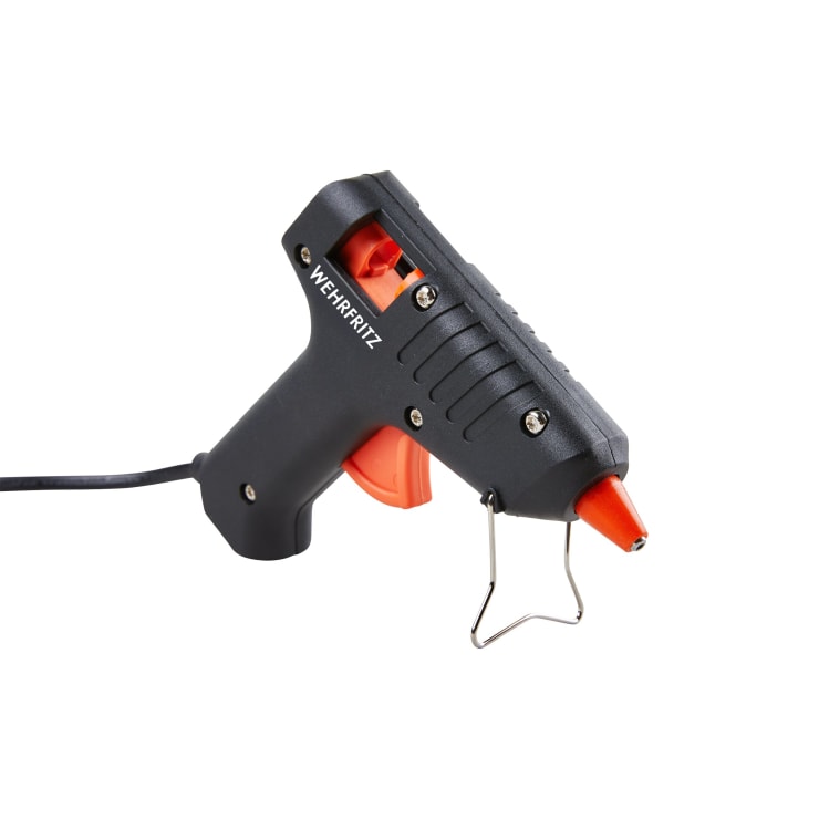 Eine schwarz-orangefarbene Heißklebepistole mit der Aufschrift HABA Pro ist auf weißem Hintergrund abgebildet, mit einem sichtbaren Netzkabel und einem Metallständer auf der Vorderseite.