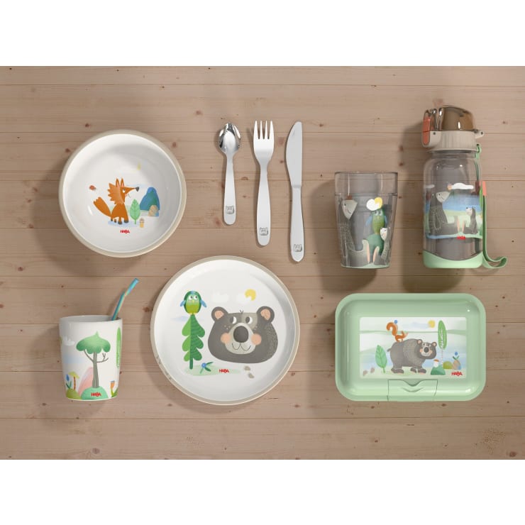Kindergeschirr mit Tiermotiven, bestehend aus Tellern, Schüsseln, einer Tasse mit Strohhalm, Besteck, einer Wasserflasche, einer Brotdose und einem Glas, alles auf einer Holzfläche angeordnet.