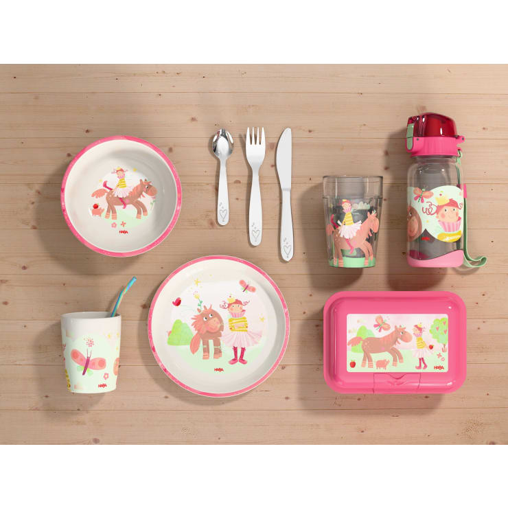 Kindergeschirr auf einer hölzernen Oberfläche, bestehend aus Tellern, Schüsseln, einer Tasse mit Strohhalm, Utensilien, einer Wasserflasche, einem Glas und einer Brotdose, alles verziert mit rosa Cartoon-Tieren und Herzen.