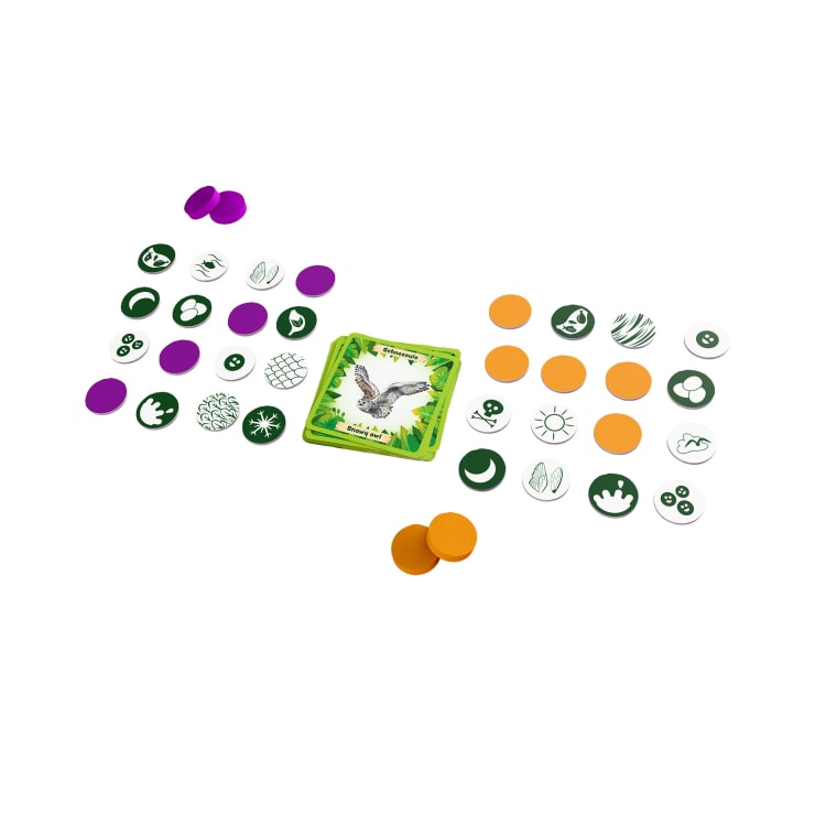 Ein Kartenspiel mit einem zentralen Stapel illustrierter Karten, umgeben von Spielsteinen und kreisförmigen Markern in Lila und Orange sowie grünen und weißen Symbolsteinen, die auf einer weißen Fläche verteilt sind.