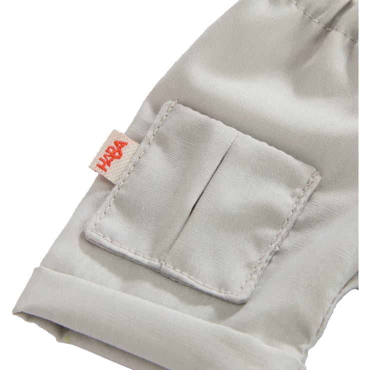Nahaufnahme einer hellgrauen Stofftasche mit sichtbaren Nähten und einem kleinen orangefarbenen Etikett mit der Aufschrift "HABA" an der Naht. Die Tasche befindet sich an einem Hosenbein oder Ärmel.