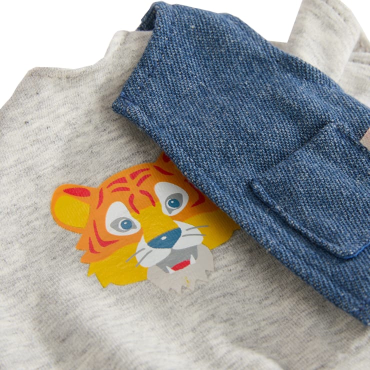 Ein grauer Stoff mit einem aufgedruckten Cartoon-Tigergesicht, der teilweise von einem blauen Jeansstoff mit einer sichtbaren Tasche bedeckt ist.