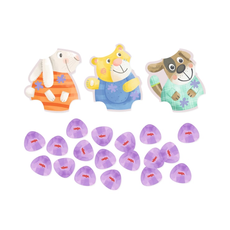 Drei Tierpuzzleteile - ein Kaninchen, ein Bär und ein Hund -, die jeweils verschiedenfarbige Kleidung tragen, sind über einer Gruppe kleiner, lila, kieselsteinähnlicher Spielsteine abgebildet, auf denen in roten Buchstaben "HABA" steht.