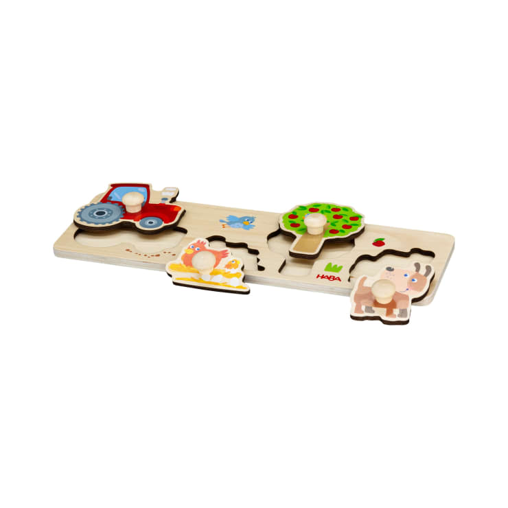 Ein Holzpuzzlebrett mit drei Teilen: ein roter Traktor, ein Baum mit grünen Blättern und roten Äpfeln und ein Elefant. Jedes Teil hat einen kleinen Knopf für eine einfache Handhabung und passende Ausschnitte auf dem Brett.