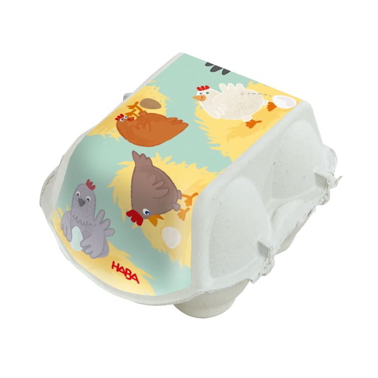 Ein Eierkarton aus weißem Karton mit einer bunten Illustration von vier Hühnern, zwei Eiern und Stroh auf dem Deckel. In der linken unteren Ecke des Deckels ist das Wort HABA in roter Farbe aufgedruckt.