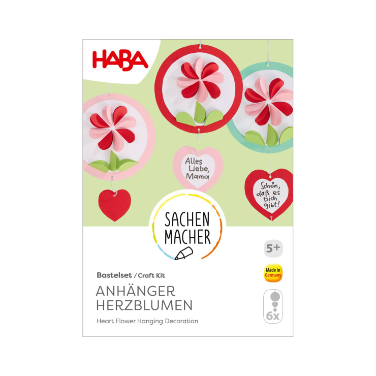 Vorderseite einer HABA-Bastelpackung mit der Aufschrift Anhänger Herzblumen, die herzförmige Blumendekorationen zeigt. Die Schachtel ist weiß mit roten Akzenten und enthält Text in Deutsch und Englisch, für Kinder ab 5 Jahren.