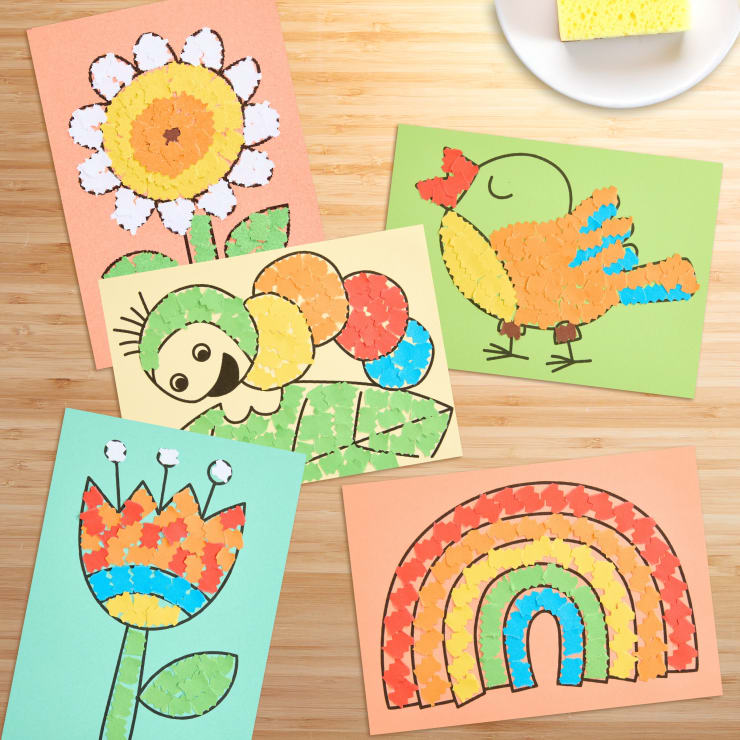 Fünf Mosaikkunstwerke aus kleinen farbigen Papierstücken auf Baupapier, die eine Blume, einen Papagei, eine Raupe auf einem Blatt, eine stilisierte Blume und einen Regenbogen darstellen und auf einer Holzoberfläche ausgestellt sind.