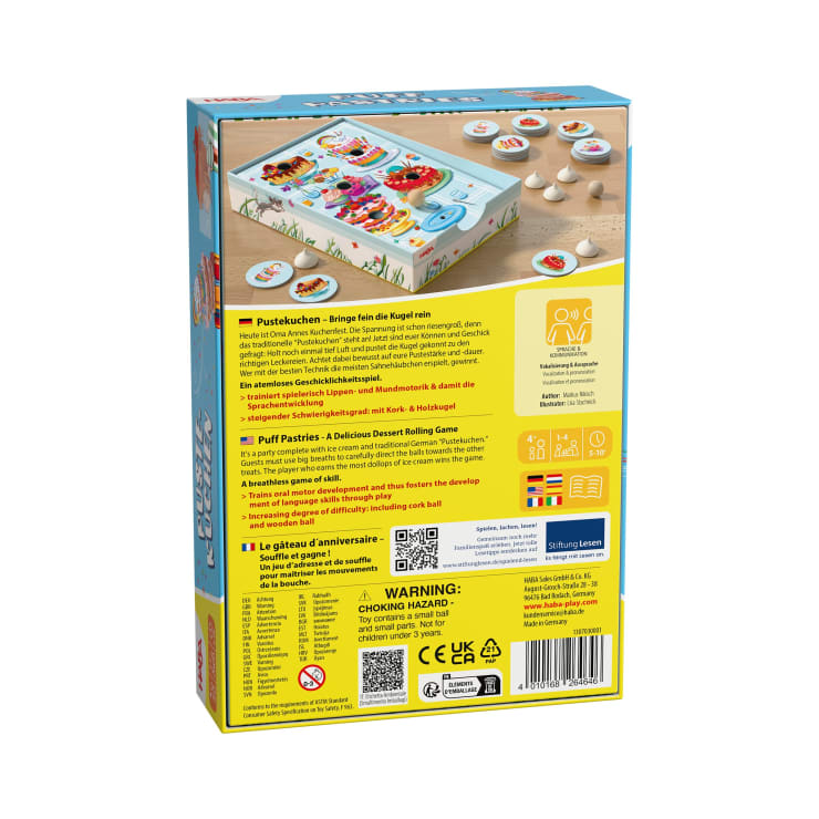Rückseite einer farbenfrohen Brettspielschachtel mit Spielkomponenten, Anleitung in Deutsch, Englisch, Französisch und Italienisch, Warnung vor Erstickungsgefahr, Sicherheitssymbolen, Strichcode und einem Foto des auf einem Tisch aufgebauten Spiels.