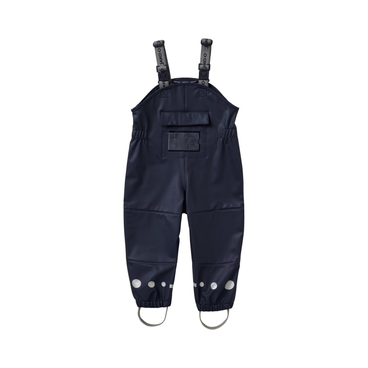 Ein dunkelblauer, wasserdichter Kinder-Overall mit verstellbaren, schwarzen Schulterriemen, einer Vordertasche, elastischen Bündchen, reflektierenden Punkten in der Nähe der Knöchel und angebrachten Steigbügeln. Der Overall ist auf einem weißen Hintergrund abgebildet.