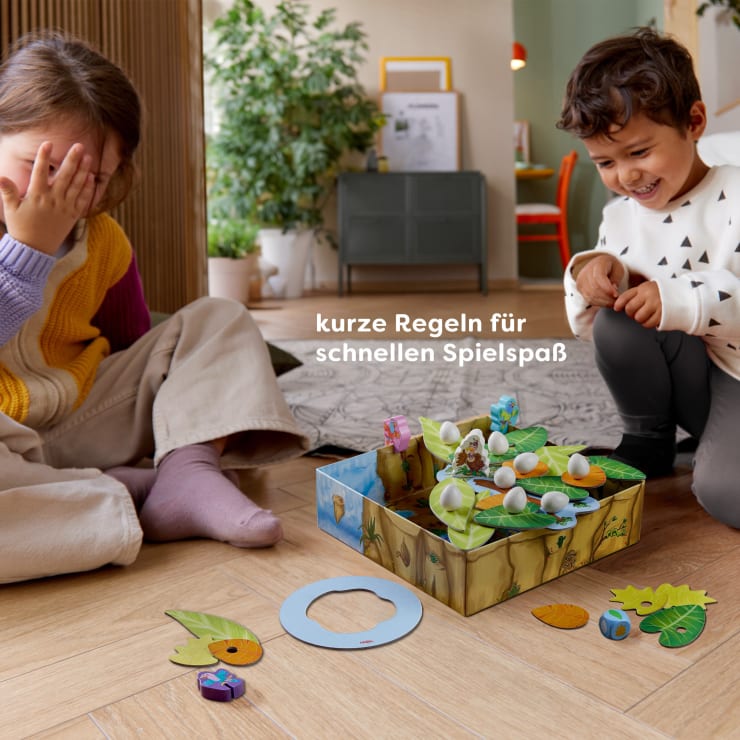 Zwei Kinder sitzen auf dem Boden und spielen ein Brettspiel mit Tier- und Eierfiguren. Ein Kind lacht, während das andere sein Gesicht bedeckt. Der deutsche Text auf dem Bild lautet: Kurze Regeln für schnellen Spielspaß.