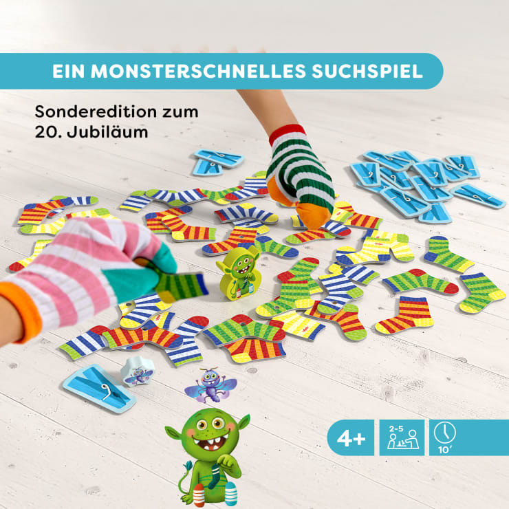 Zwei Kinderhände in bunt gestreiften Handschuhen spielen ein Spiel mit gestreiften Puzzleteilen auf einem weißen Boden. Das Bild enthält deutschen Text und Cartoon-Monster, die darauf hinweisen, dass das Spiel für Kinder ab 4 Jahren geeignet ist.