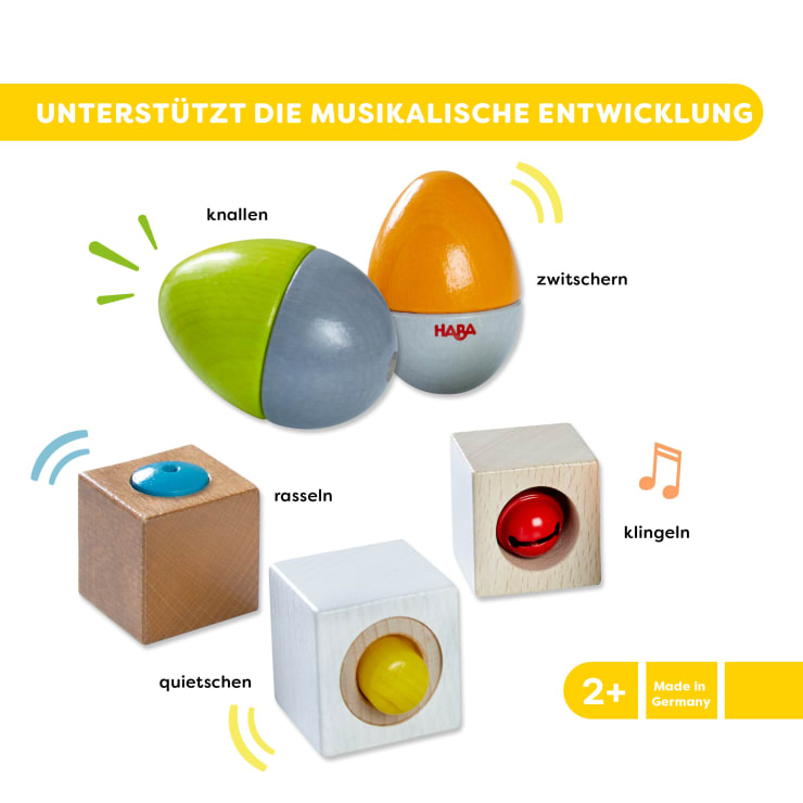 Ein Set mit fünf musikalischen Holzspielzeugen für Kinder, die jeweils mit ihrem deutschen Klang beschriftet sind, einschließlich einer Ei-Form und vier Würfeln mit Knöpfen, dargestellt auf weißem Hintergrund mit gelben Akzenten und Altersempfehlung 2+.
