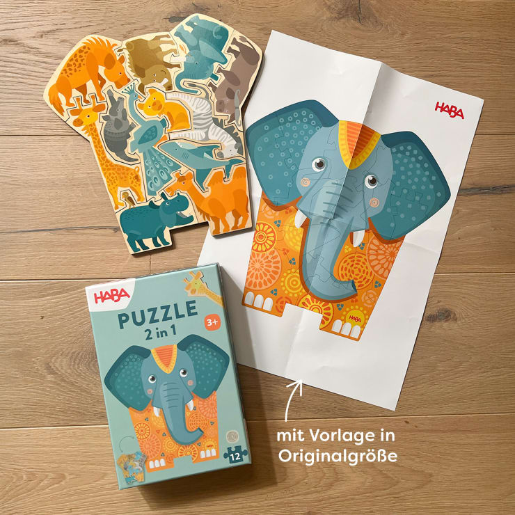 Ein Kinderpuzzle mit tierischen Teilen, ein illustriertes Elefantenposter und die HABA-Box mit der Aufschrift Puzzle 2 in 1 sind auf einer Holzfläche angeordnet. Ein deutscher Text weist auf das Plakat hin.