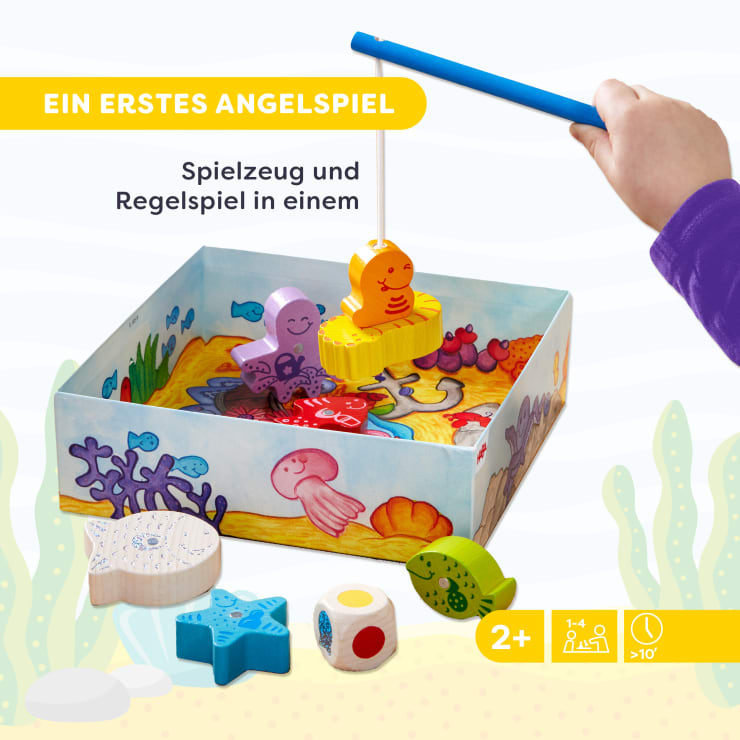 Eine Kinderhand hält eine blaue Angelrute über einer Schachtel mit buntem Meerestierspielzeug und einem Würfel. Der deutsche Text lautet Ein erstes Angelspiel und Spielzeug und Regelspiel in einem. Das Spiel ist für Kinder ab 2 Jahren, für 1-4 Spieler.