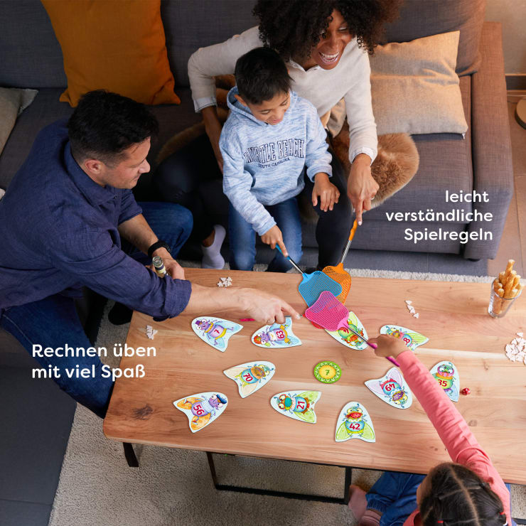Eine vierköpfige Familie sitzt an einem Holztisch und spielt ein pädagogisches Kartenspiel. Die Kinder benutzen Fliegenklatschen, um die Karten zu treffen. Der Text auf Deutsch lautet: "Rechnen üben mit viel Spaß und leicht verständlichen Spielregeln.