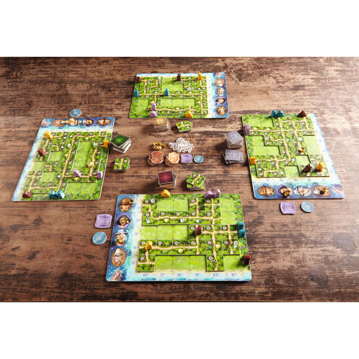 Vier farbenfrohe Spielbretter mit illustrierten Kacheln, Karten, Spielsteinen und Spielfiguren sind auf einem Holztisch für ein Tabletop-Brettspiel angeordnet. Die Spielbretter sind mit grünen Pfaden versehen, und die Komponenten sind für das Spiel übersichtlich angeordnet.