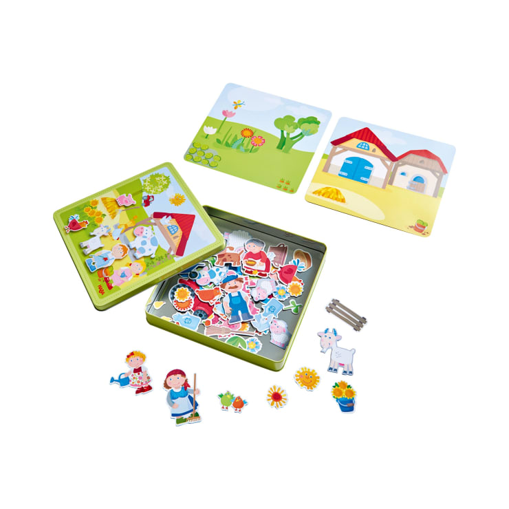 Ein magnetisches Kinderspielset mit einer offenen grünen Blechdose, die bunte Magnetteile, zwei illustrierte Hintergrundtafeln und verschiedene magnetische Figuren, Tiere und Pflanzen enthält, die um die Dose herum angeordnet sind.