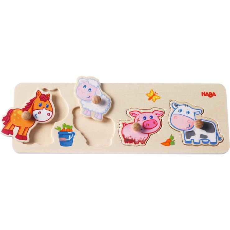 Ein Tierpuzzle aus Holz mit drei Teilen: ein Pferd, ein Schaf, ein Schwein und eine Kuh. Jedes Teil hat einen Knopf für eine einfache Handhabung. Auf dem Brett sind außerdem eine Karotte, ein Schmetterling und ein Eimer mit Gemüse abgebildet.