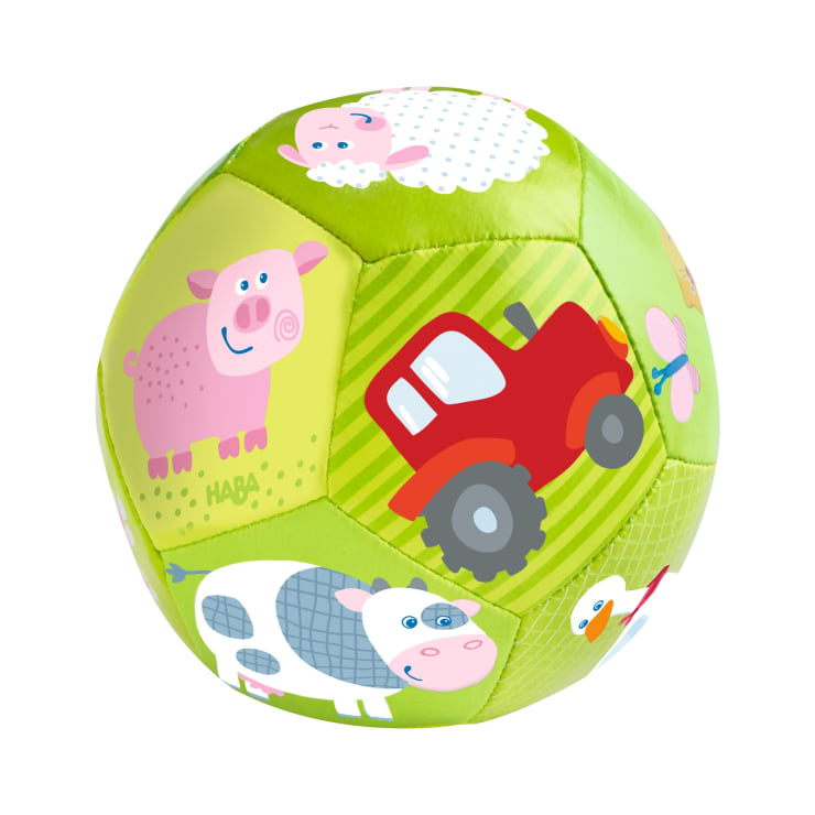 Ein weicher grüner Ball mit Illustrationen von Schwein, Schaf, Kuh, Ente, Schmetterling und rotem Traktor auf hellgrünem Hintergrund.