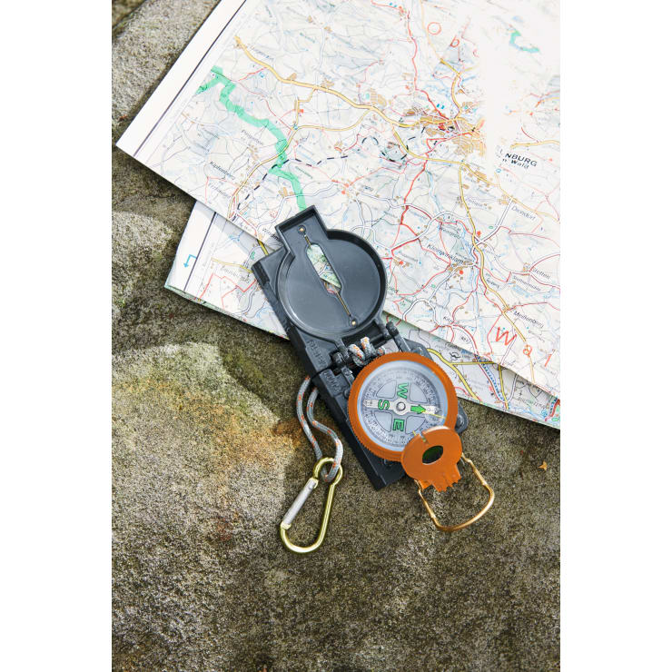 Eine topografische Karte und ein schwarz-orangefarbener Kompass mit Umhängeband und Karabiner werden auf eine Steinfläche gelegt.