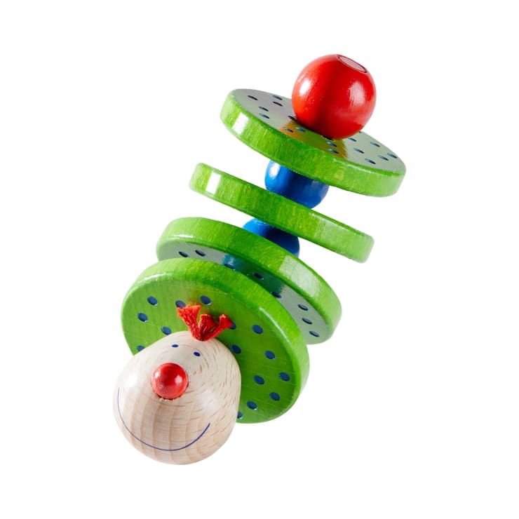 Ein Holzspielzeug mit grünen Scheiben, blauen Tupfen, einem roten Ball oben und einem runden Kopf unten, der ein lächelndes Gesicht mit roter Nase und rotem Garnhaar zeigt, auf weißem Hintergrund.
