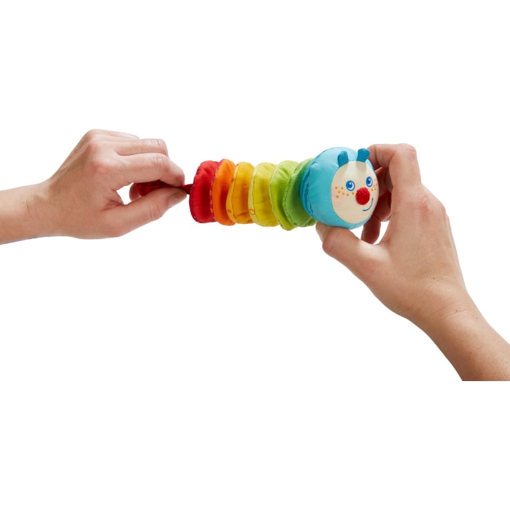 Zwei Hände ziehen eine bunte, ziehharmonikaförmige Raupe mit Plüschkopf und blauen Fühlern auseinander. Die Körpersegmente sind rot, orange, gelb, grün und hellgrün.