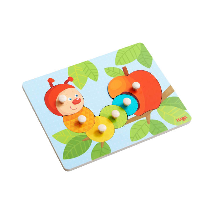 Ein Holzpuzzle mit einer lächelnden Raupe auf einem Ast mit einem Apfel. Die Puzzleteile sind rund und haben kleine Noppen zum einfachen Greifen. Der Hintergrund zeigt grüne Blätter auf einer hellblauen Fläche.