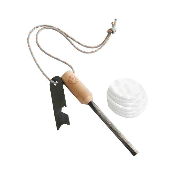 Ein Feuerstarter-Set mit einem Holzgriff, einem angebrachten Metallstarter und einer bunten Schnur. Vier runde Wattepads sind in der Nähe auf einem weißen Hintergrund platziert.