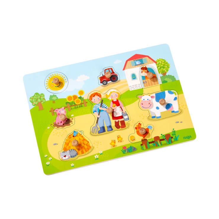 Ein farbenfrohes Holzpuzzle zeigt eine Bauernhofszene mit herausnehmbaren Teilen in Form eines Bauern, einer Bäuerin, einer Kuh, eines Schweins, einer Katze, eines Huhns und eines Traktors vor dem Hintergrund einer Scheune und von Feldern.