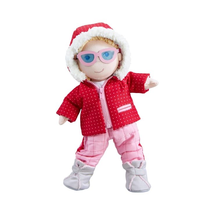 Eine Stoffpuppe, die eine rote Kapuzenjacke mit weißem Saum, eine rosa Hose, hellgraue Stiefel und eine rosa Brille trägt und auf einem weißen Hintergrund steht.