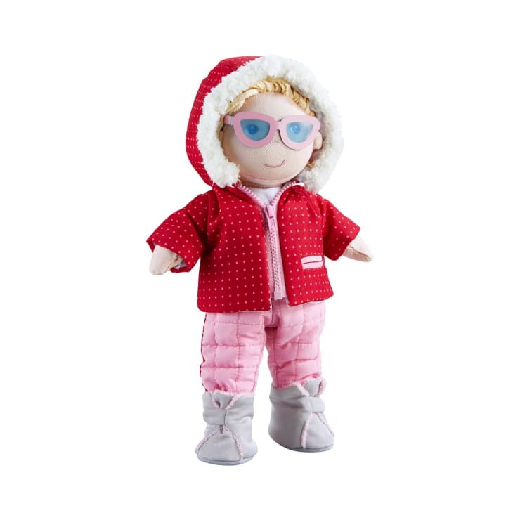 Eine Plüschpuppe, die eine rote Kapuzenjacke mit weißen Punkten, eine rosa Hose, graue Stiefel und eine lila Sonnenbrille trägt. Die Puppe hat helles Haar und ein lächelndes Gesicht.