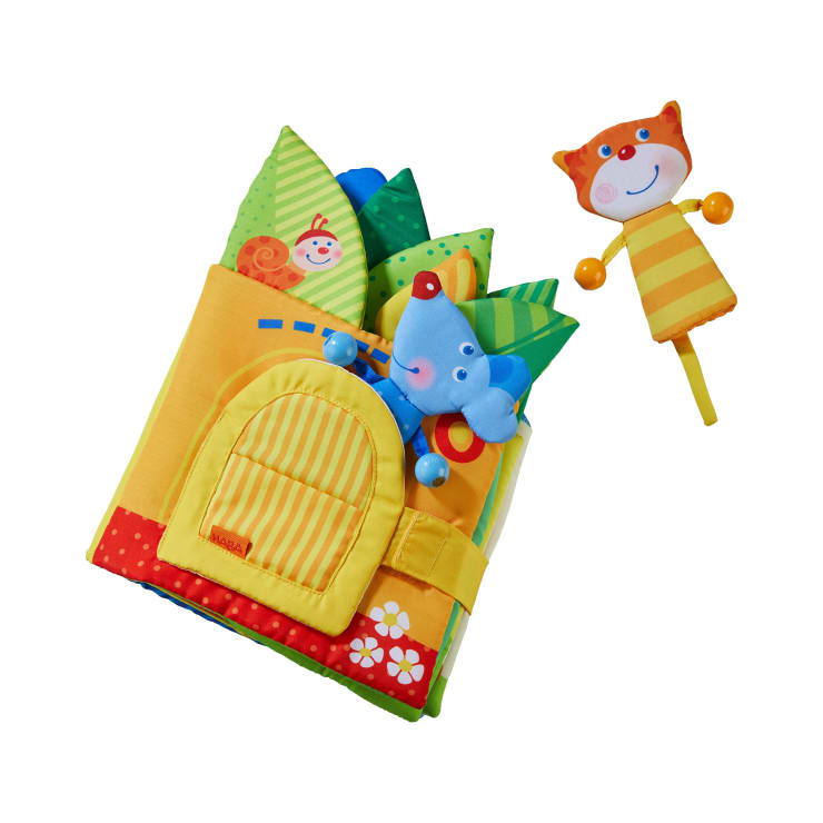 Ein farbenfrohes Buch aus weichem Stoff mit einer gelben Tasche, grünen und blauen Blättern, einer blauen Plüschmaus und einer separaten orange-gelben Katzenfigur aus Plüsch mit einem Stiel.