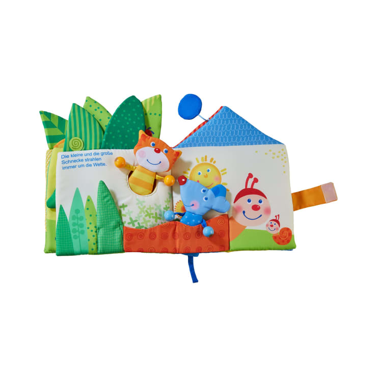 Ein farbenfrohes Stoff-Babybuch mit verschiedenen Texturen, Mustern und Tierfiguren, darunter eine Katze, eine Maus und eine Sonne. Auf einer Seite gibt es grüne Blätter, eine Hausform und einen deutschen Text.