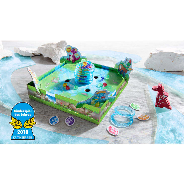 Ein farbenfrohes Kinderbrettspiel mit einem grünen Schachtelboden, einem zentralen Plastikbienenstock, bunten Edelsteinen, Dinosaurierfiguren aus Pappe, Spielplättchen und einem blauen "Kinderspiel des Jahres 2018"-Abzeichen unten links.