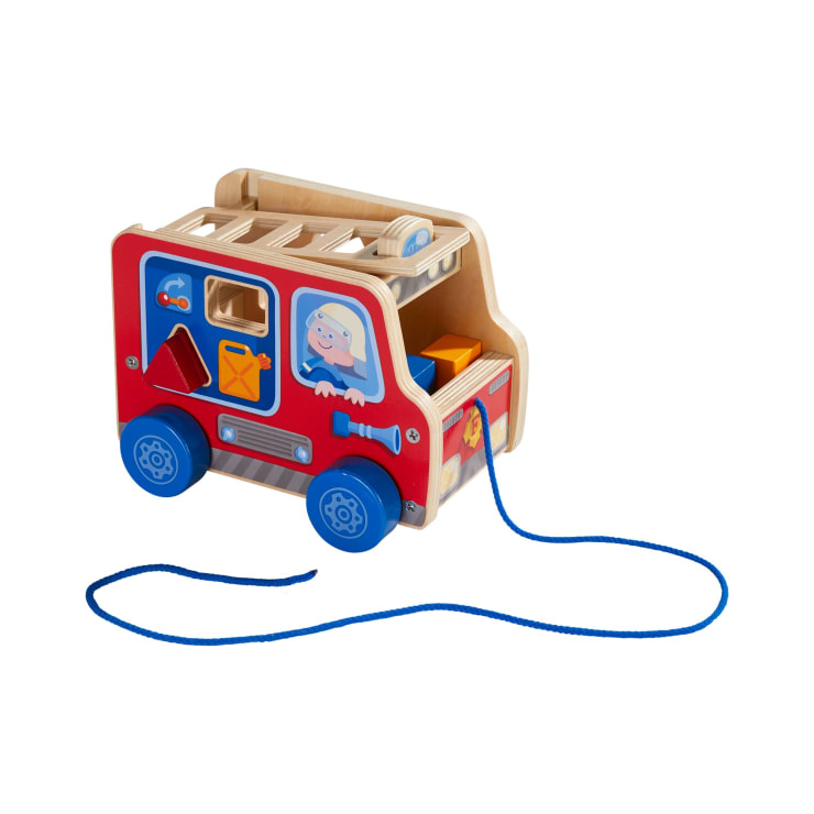 Ein nachziehbarer Spielzeug-LKW aus Holz mit blauen Rädern, roten Seiten und einer blauen Schnur. Der Lastwagen hat Löcher zum Sortieren von Formen und bunte Blöcke und auf einer Seite ist eine Cartoon-Person abgebildet.