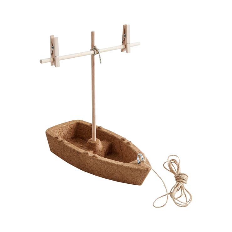Ein kleines Modellboot aus Kork mit einem hölzernen Mast und einem Querbalken, zwei Wäscheklammern, die am Querbalken befestigt sind, und einem Stück Schnur, das neben dem Boot aufgerollt ist. Der Hintergrund ist einfarbig weiß.