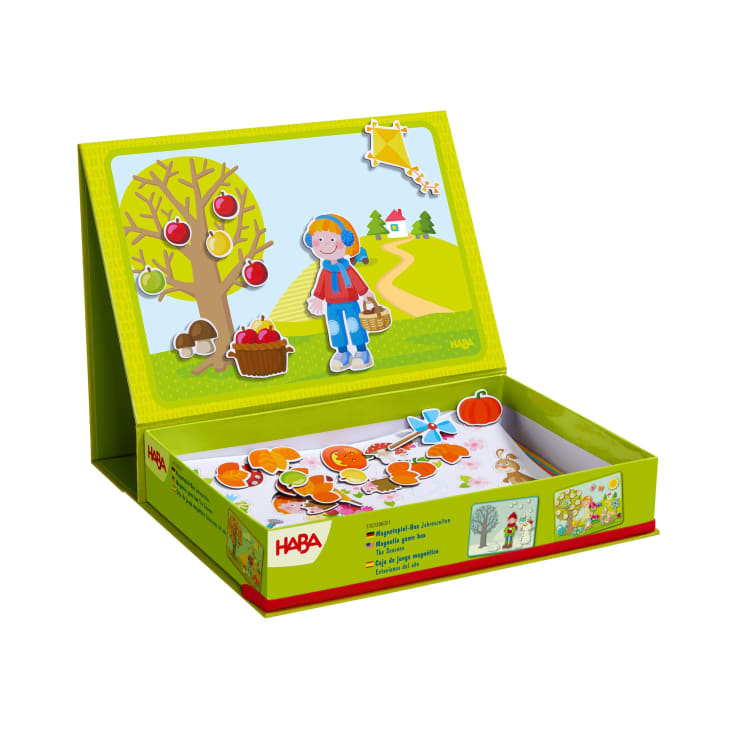Ein magnetisches Spielset mit einer stehenden Tafel, die ein Mädchen, einen Baum mit Äpfeln, Pilzen und einen Korb zeigt. Lose Magnetteile, darunter Früchte und Blätter, befinden sich in der offenen Schachtel darunter. Die Marke HABA ist auf der Schachtel sichtbar.