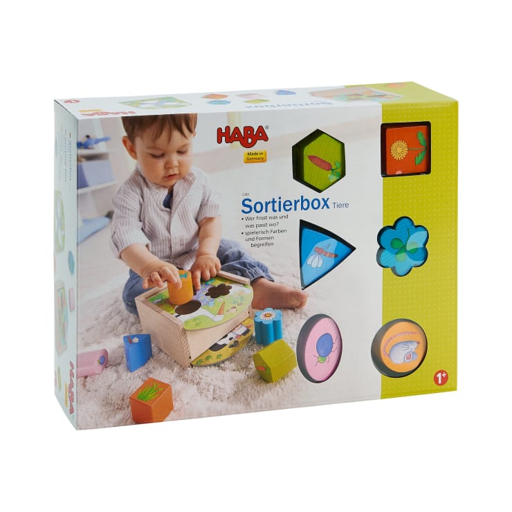 Ein Kleinkind spielt mit der HABA Sortierbox Tiere. Auf der Schachtel sind bunte Tierformen und Illustrationen abgebildet. Die Altersempfehlung für 1 Jahr und älter ist in der unteren rechten Ecke angegeben.