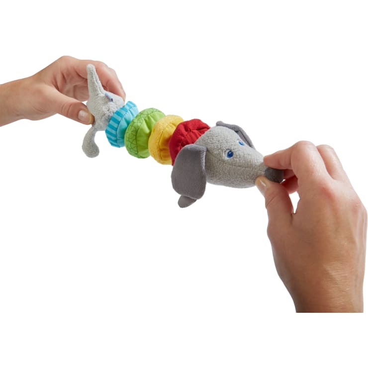 Zwei Hände halten und strecken ein buntes Plüschtier in Form eines Elefanten mit regenbogenfarbenen Stoffringen zwischen Kopf und Körper, isoliert auf einem weißen Hintergrund.