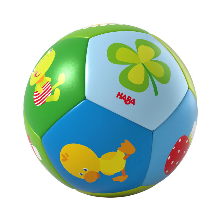 Ein farbenfroher Kinderball mit Illustrationen von einem Frosch, einem Küken, einem vierblättrigen Kleeblatt und einem roten Pilz auf den Seiten. Der Ball ist aus Stoff gefertigt und trägt den Markennamen HABA.