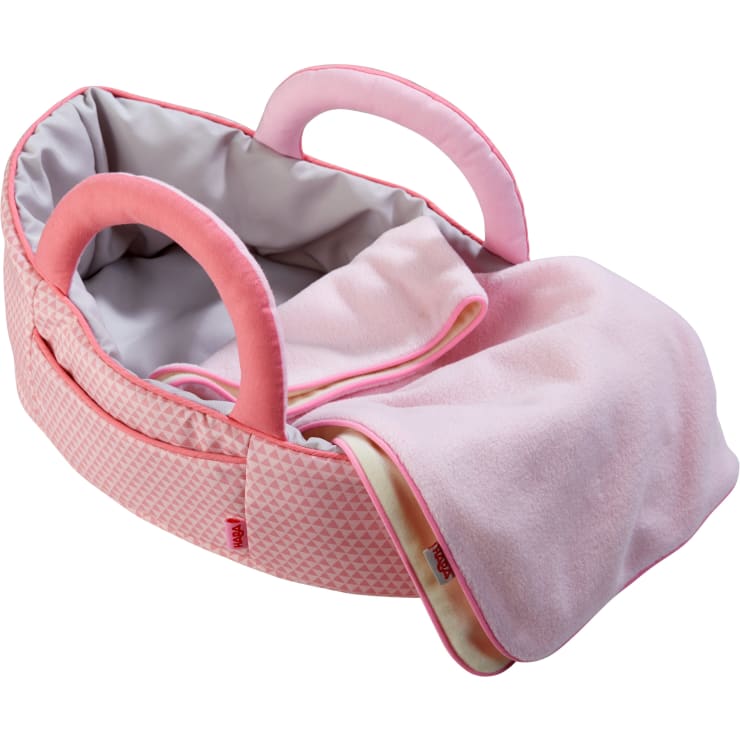 Eine weiche rosa-beige Puppentasche mit zwei gepolsterten Griffen, gefüttertem Innenraum und einer passenden rosa Decke. Die Puppentasche ist mit einem dezenten geometrischen Muster und kleinen roten Anhängern verziert.