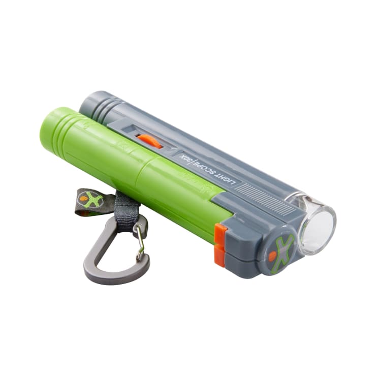 Eine kompakte, grau-grüne Taschenlampe mit einem orangefarbenen Schalter, einer klaren Linse, einem schwarzen Karabinerhaken und einer kleinen Schlaufe an einem Ende, abgebildet vor einem weißen Hintergrund.